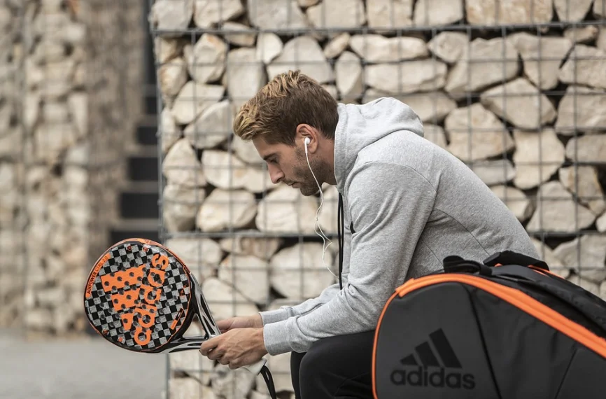 Homem sentado com raquete e bolsa da adidas, fazendo referência a comprar ações da Adidas.