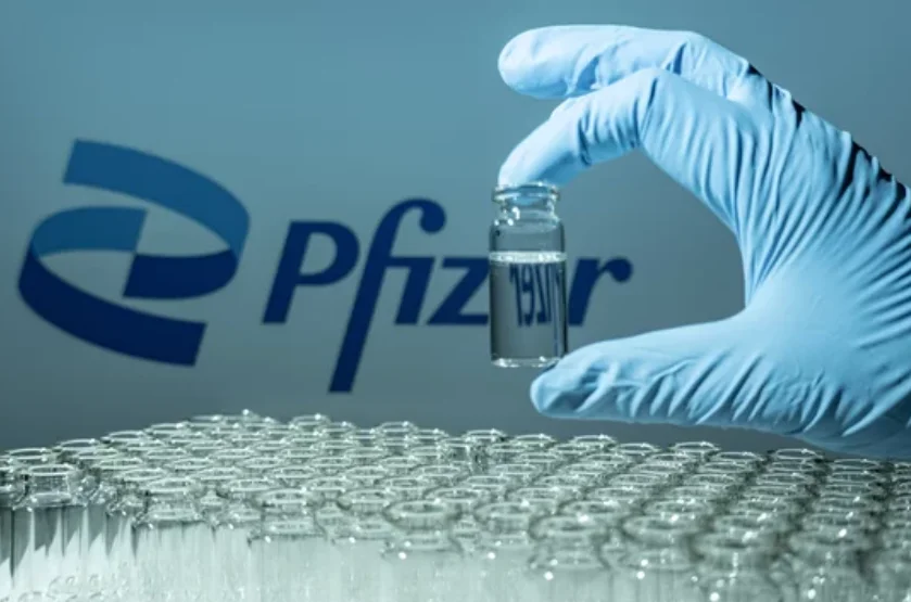 Imagem de uma mãe com luva segurando uma ampola, ao fundo logo com escrita da Pfizer ao fundo, fazendo referência a comprar ações da Pfizer.