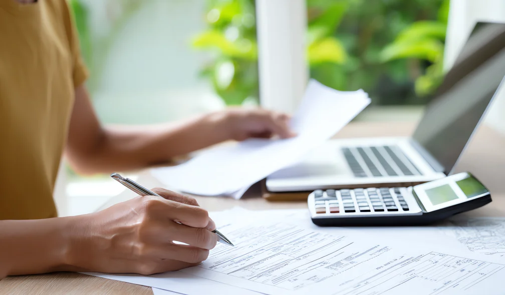 Taxa selic: mulher analisando documentos financeiros com calculadora e notebook.